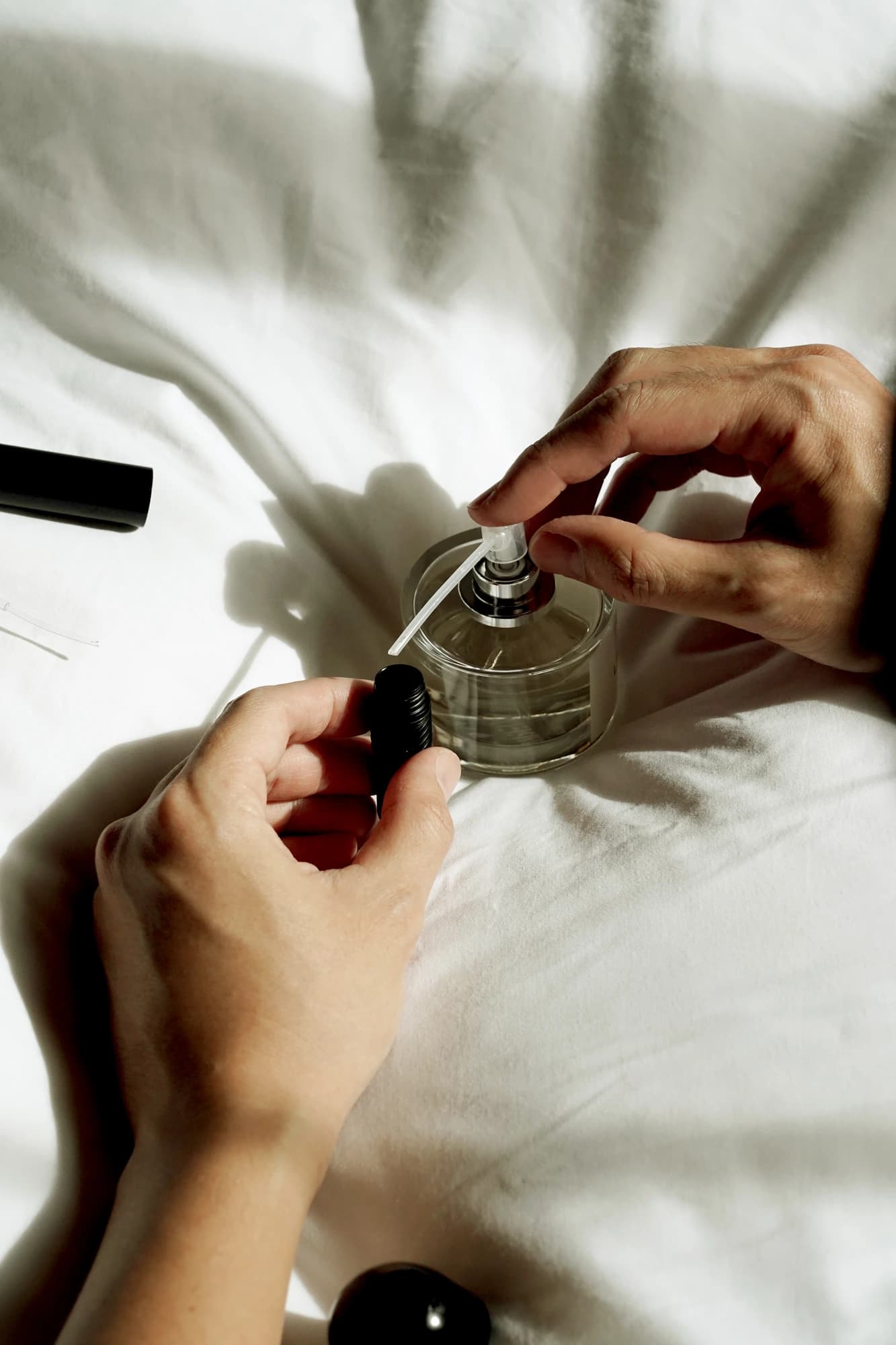 Hands filling the Mordeco nanoSprayer from a perfume bottle pump, soft natural light on white linen, easy refill