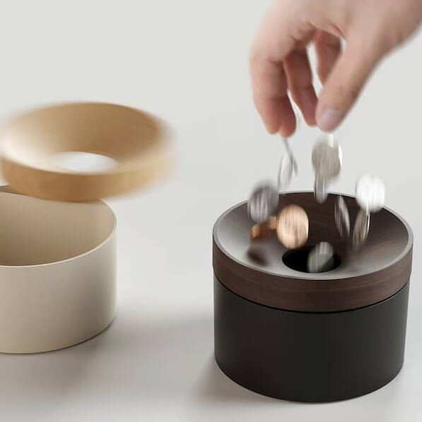 Hand dropping coins into the Revov Coin Storage beech-wood lid